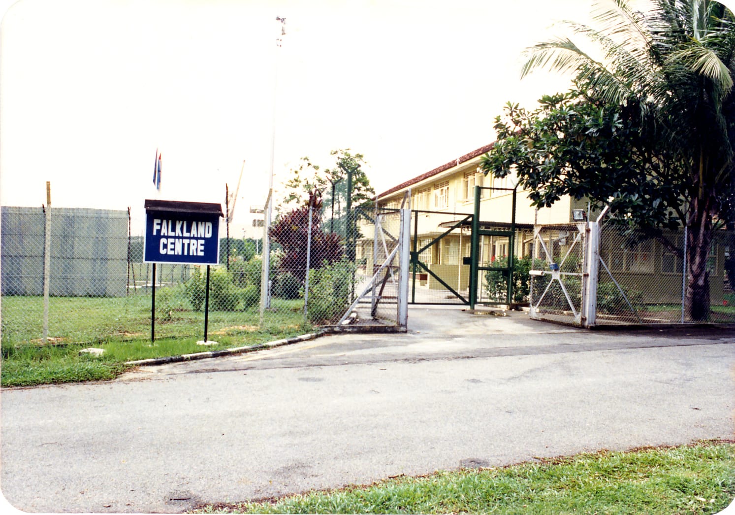 Sign reading "Falkland Centre" in front of a fenced compound with a building and trees.